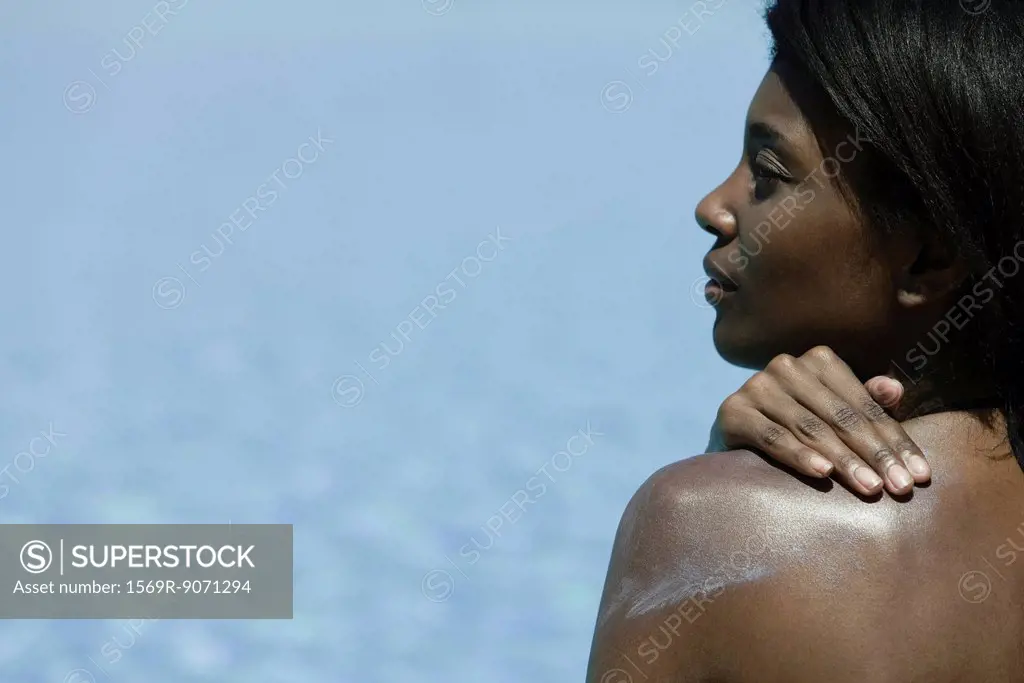 Woman applying sunblock to shoulder, rear view