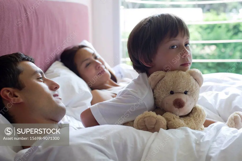 Boy sitting in bed with his parents and his teddy bear