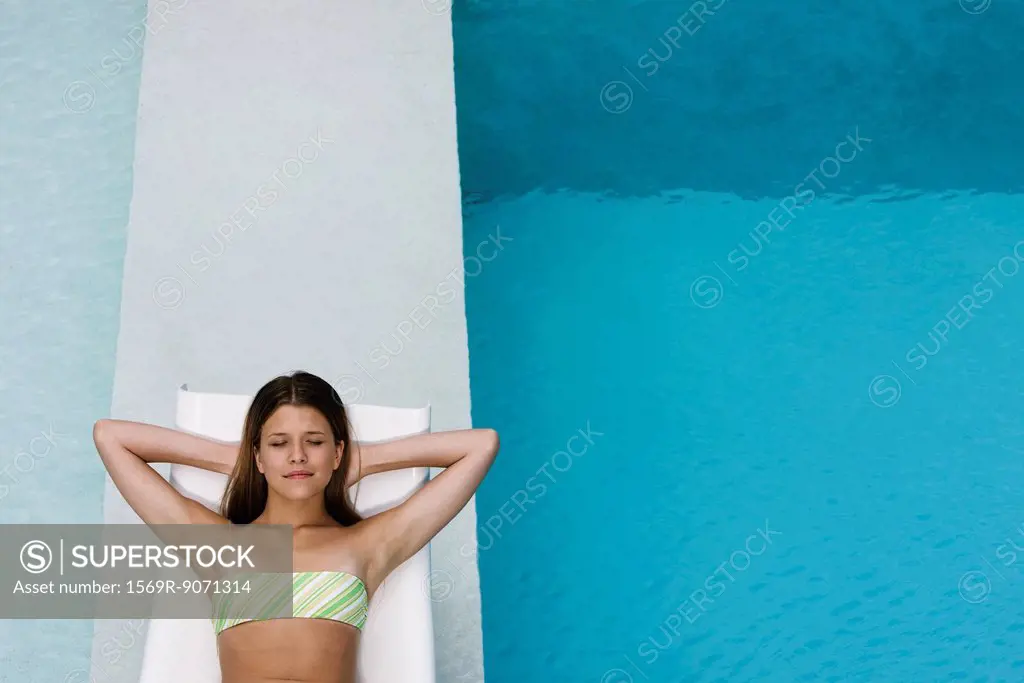 Young woman contentedly reclining on poolside deckchair