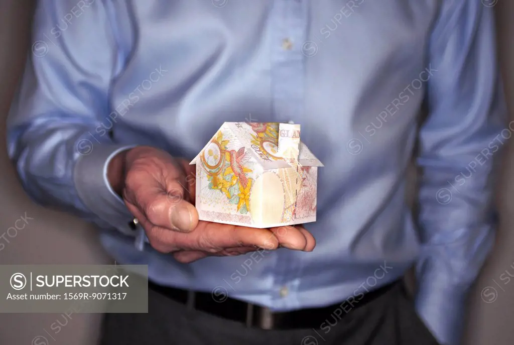 Man holding model house folded with British pound banknote, mid section