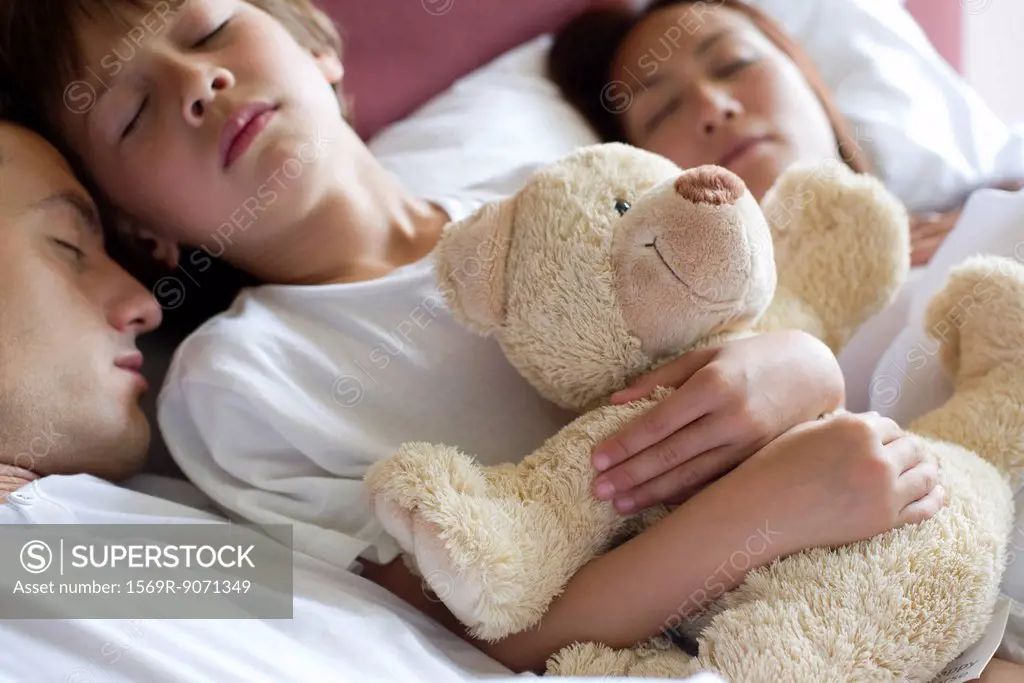 Boy sleeping in bed with his parents, holding teddy bear