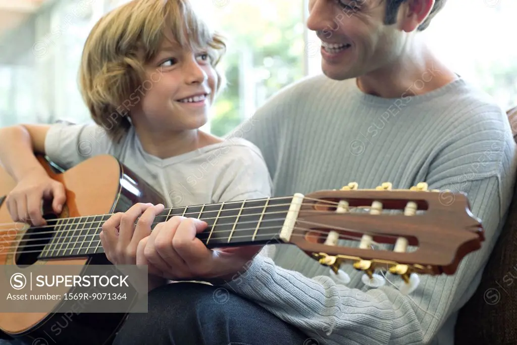 Boy learning how to play guitar with father