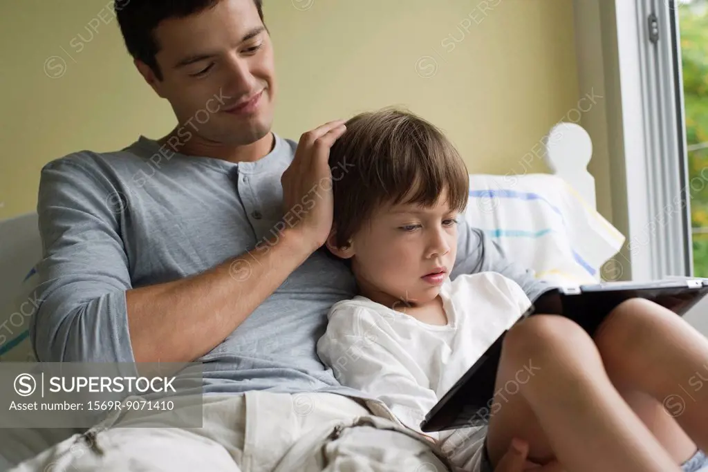 Father and son relaxing together with electronic book