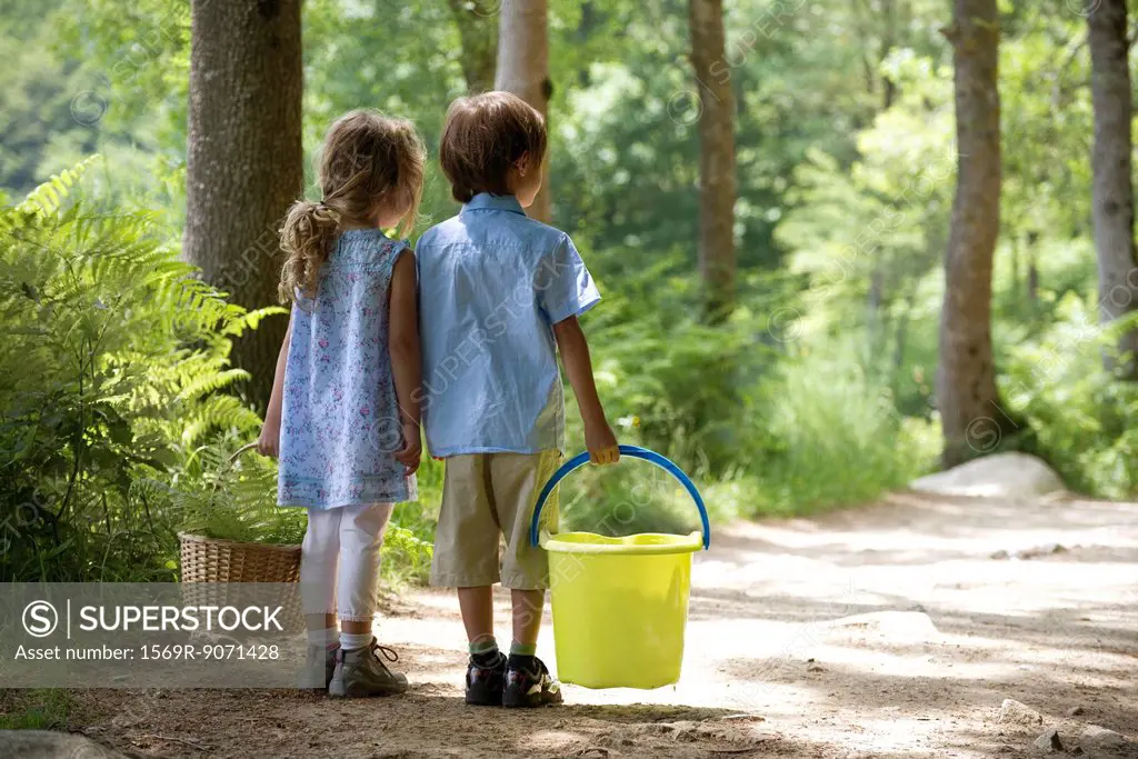Children together on path in woods, girl carry basket and boy carrying bucket