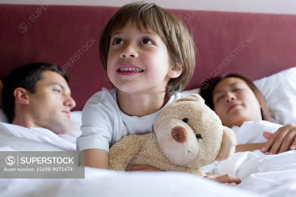 Boy sitting in parents´ bed, hugging teddy bear