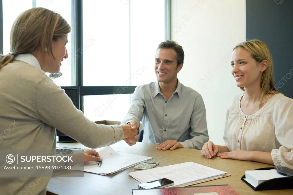 Couple shaking hands with businesswoman in office