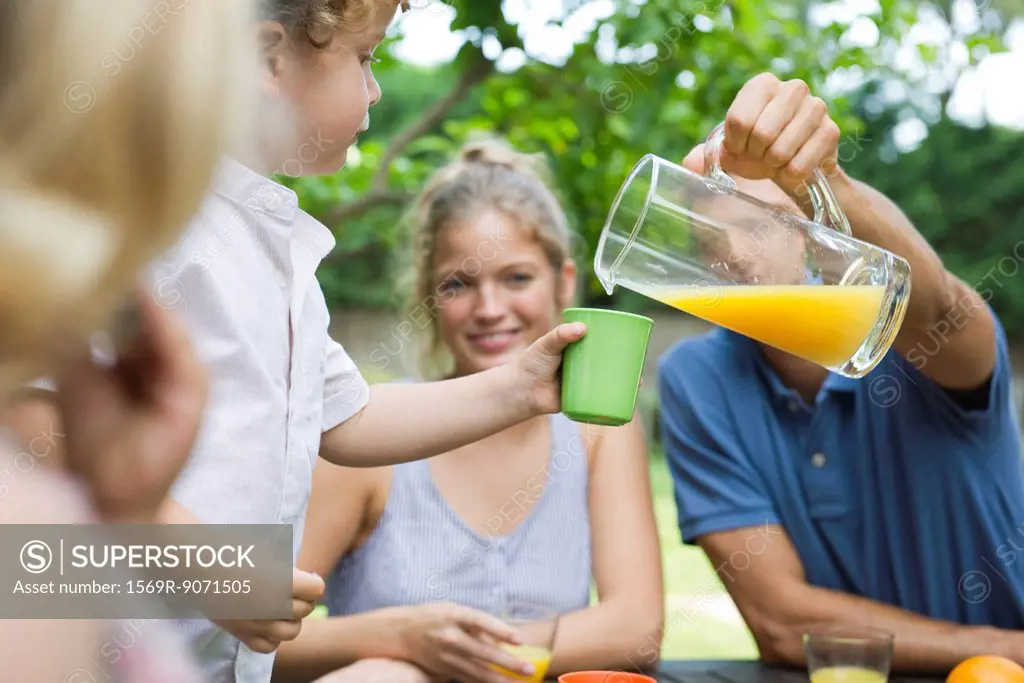 Family together outdoors, father pouring glass of juice for son