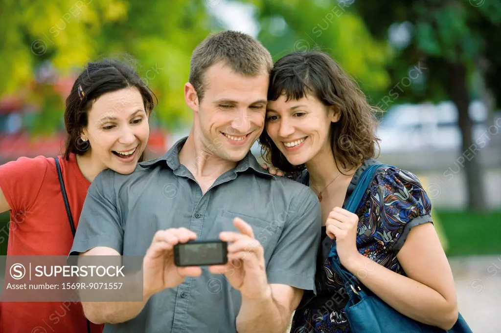 Man photographing himself with two female friends using cell phone