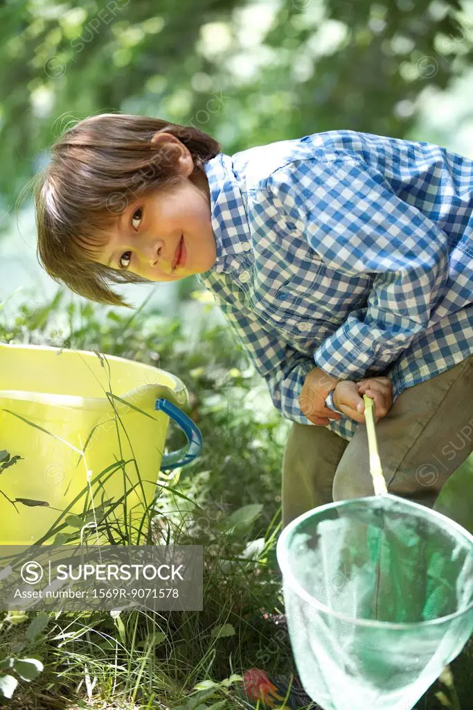 Boy leaning over bucket with fishing net in hands
