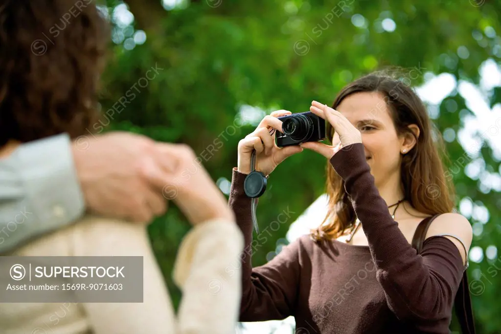 Woman photographing couple with digital camera, over the shoulder view