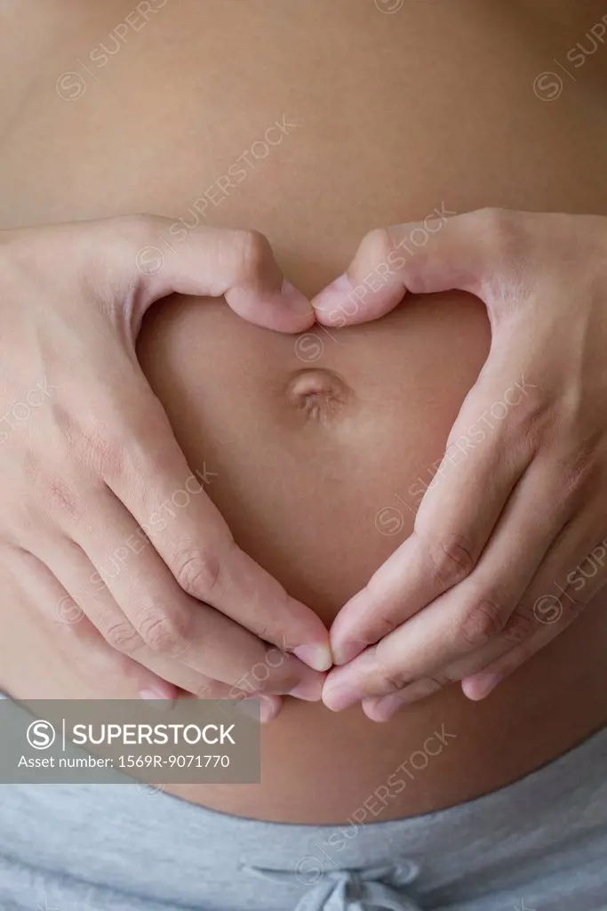 Pregnant woman´s hands making heart shape on her belly, cropped