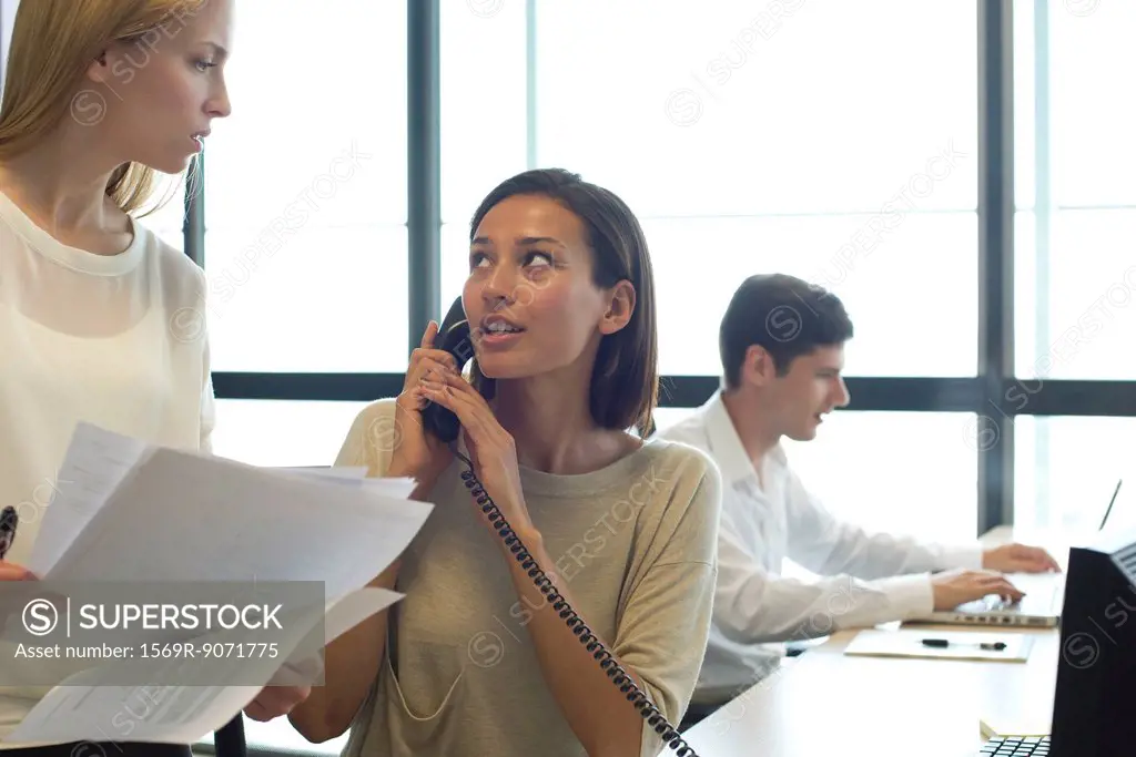 Businesswoman talking on phone in office, looking at colleague
