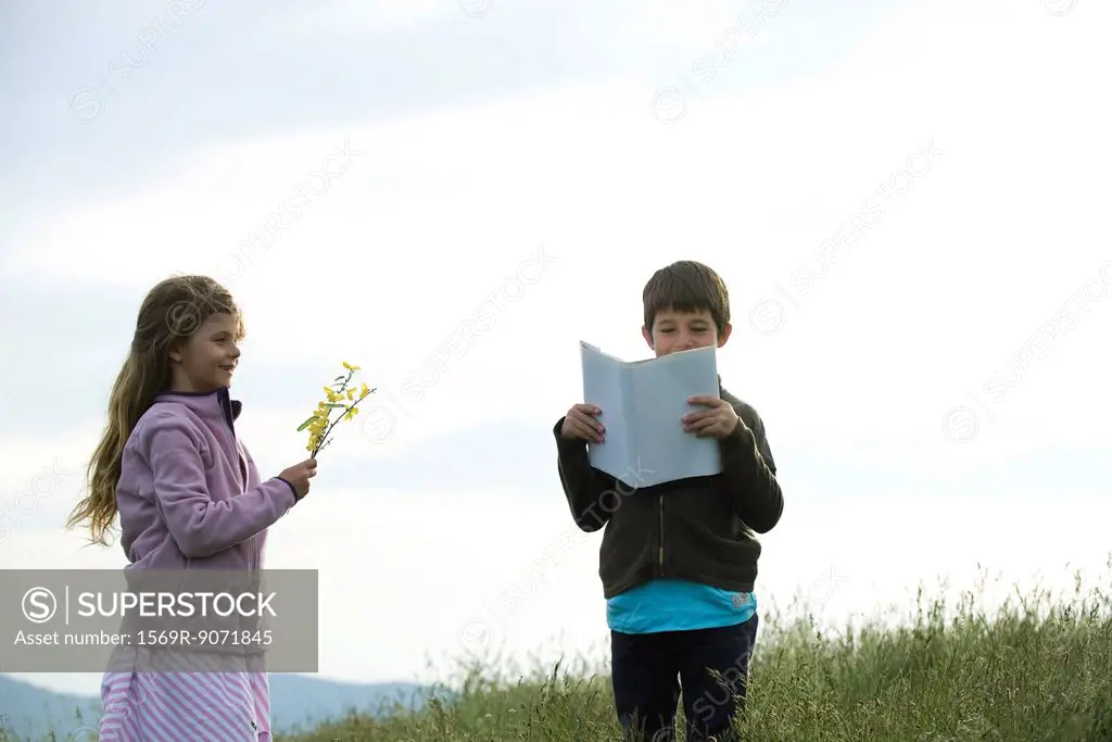 Children in field, boy reading book while girl picks wildflowers