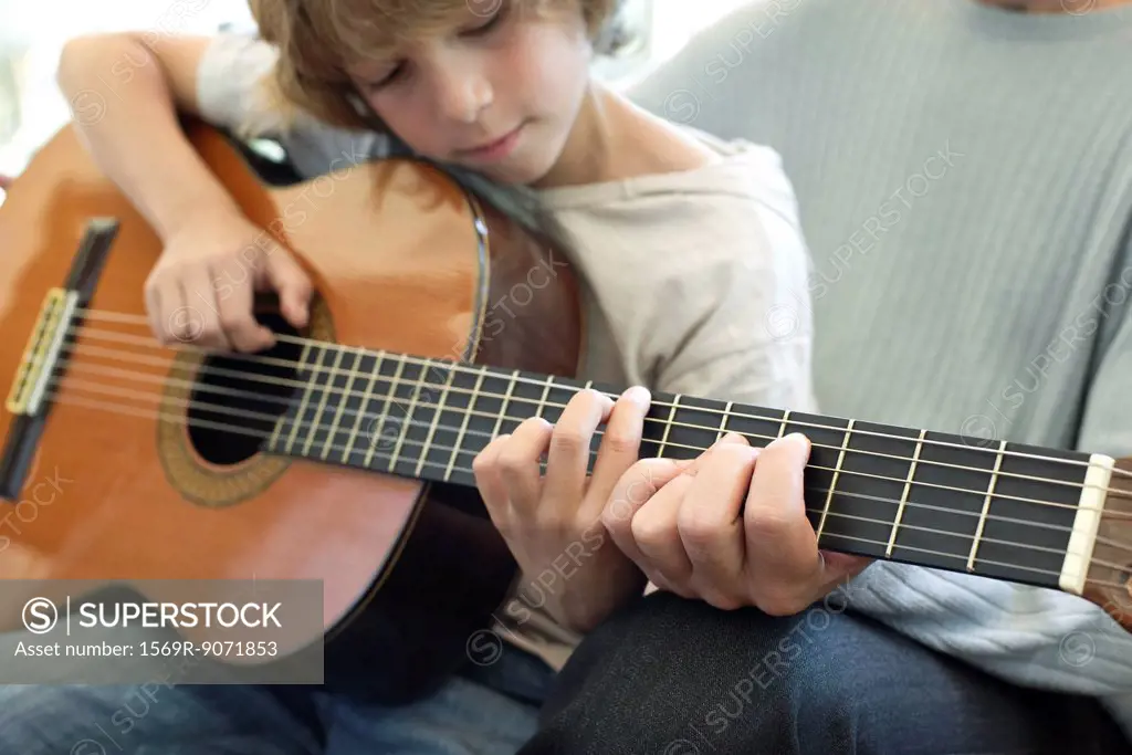Boy learning how to play guitar with father