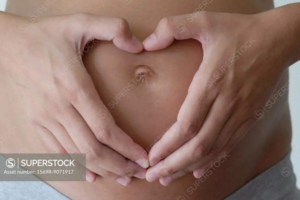 Pregnant woman´s hands making heart shape on her belly, cropped