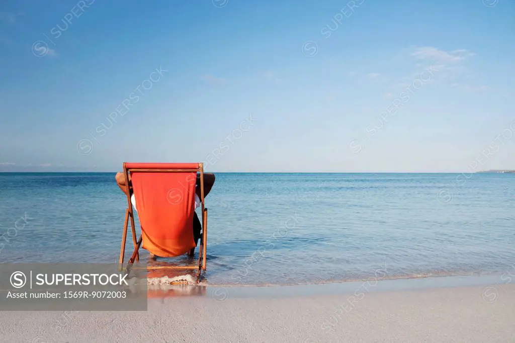 Man sitting in deckchair looking at ocean, rear view