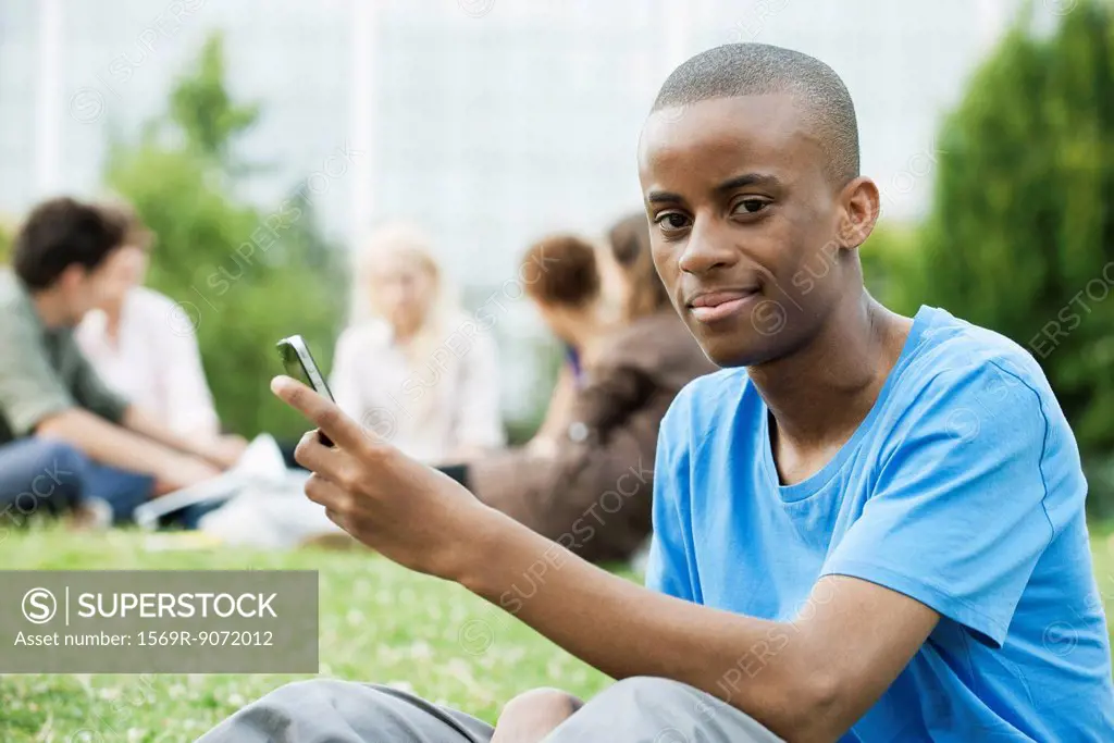 Young man with cell phone, people in background, portrait