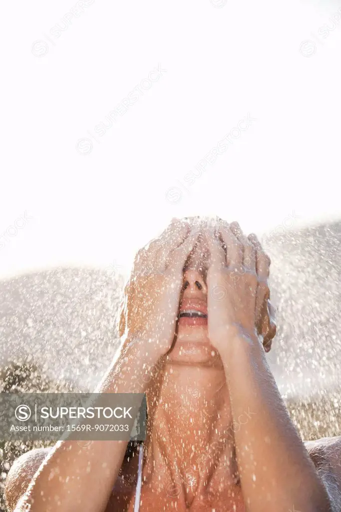 Woman washing face under shower outdoors