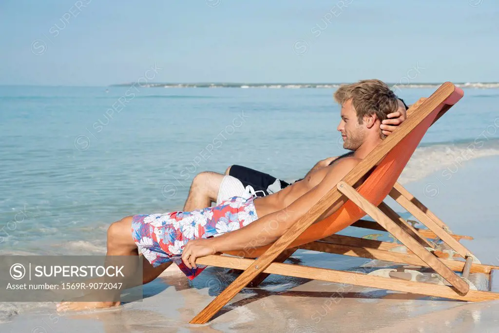 Two men sitting side by side on beach looking at ocean