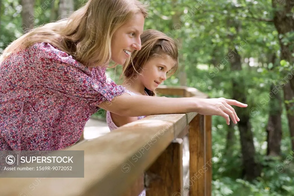 Mother and young daughter looking over railing together