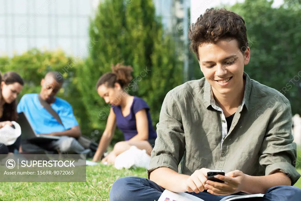 Young man text messaging with cell phone, group of people in background