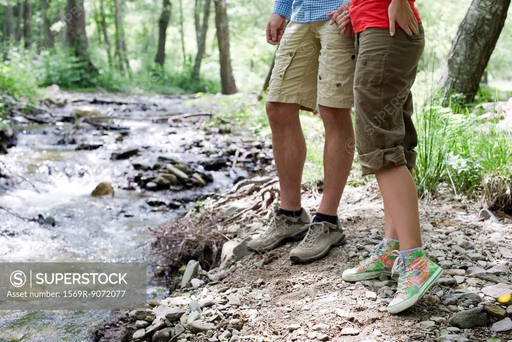 Couple hiking along stream in woods, low section