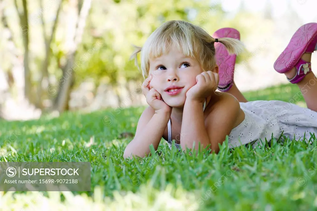 Little girl lying on grass, looking up