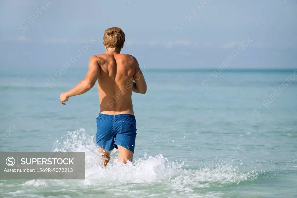 Barechested man running in water, rear view