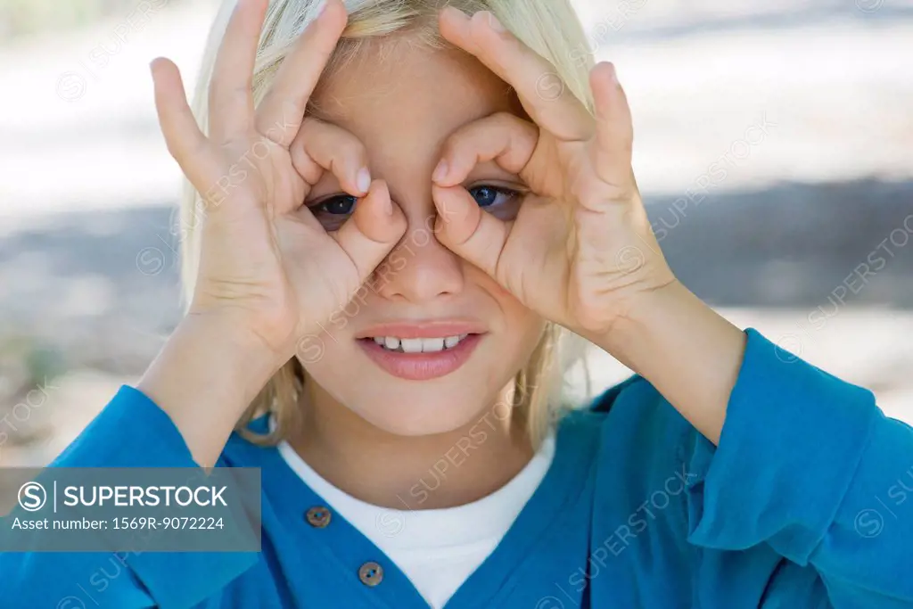 Boy forming circles with fingers around eyes