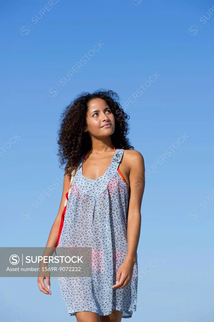 Woman in sundress walking outdoors, looking up and smiling