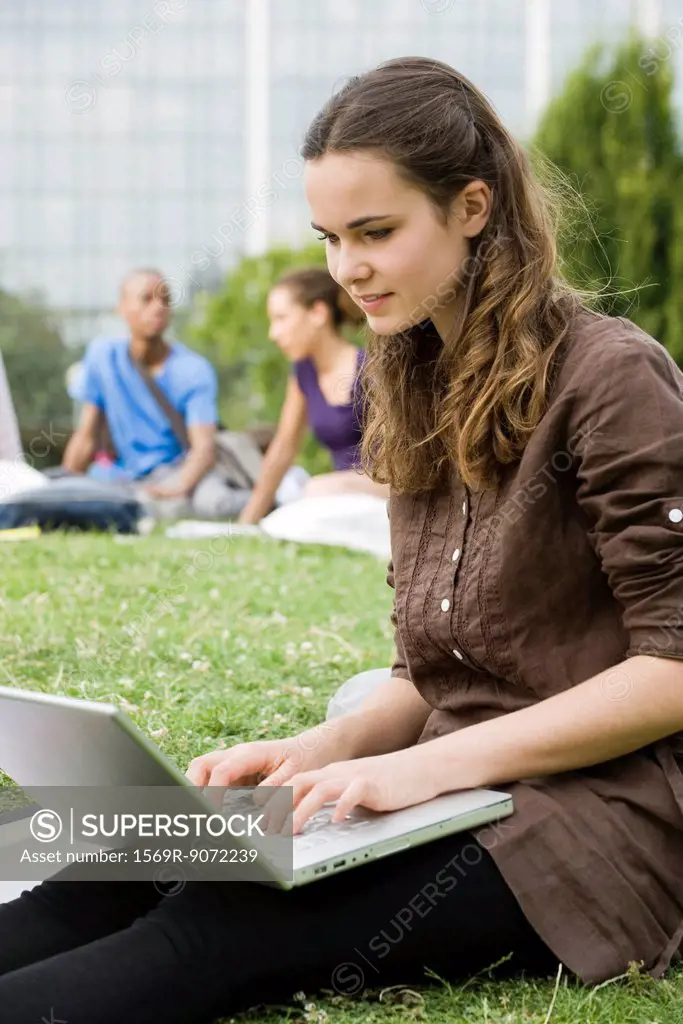 Young woman using laptop computer outdoors, people in background, portrait