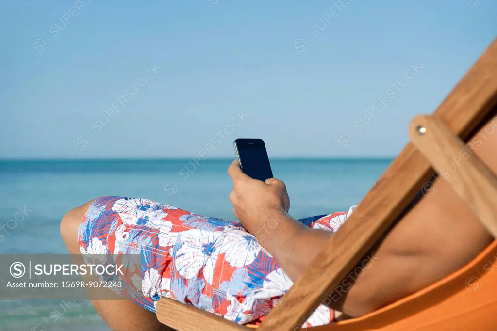 Man using cell phone while sitting on beach, cropped