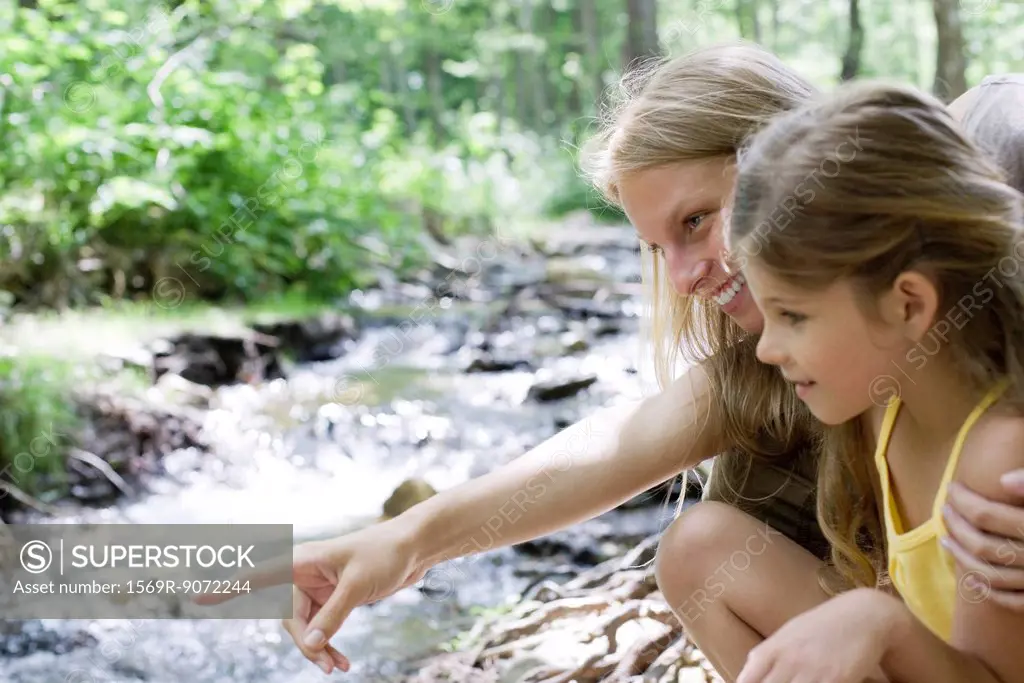 Mother and daughter looking at stream in woods