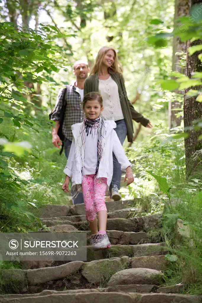 Girl walking down stone steps in woods, parents in background