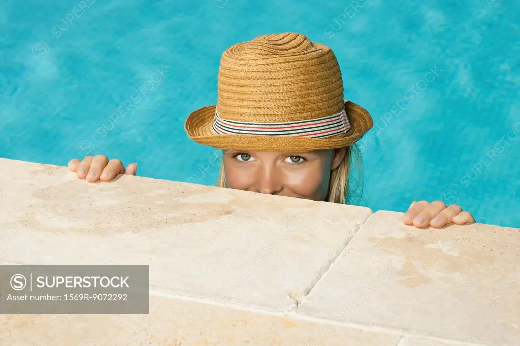 Woman in pool, peeking over edge at camera