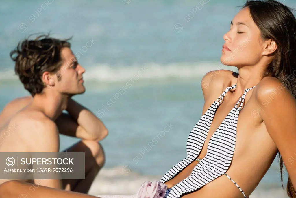Young woman relaxing on beach, boyfriend in background