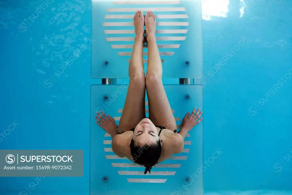 Woman relaxing on swimming pool footbridge smiling up at camera