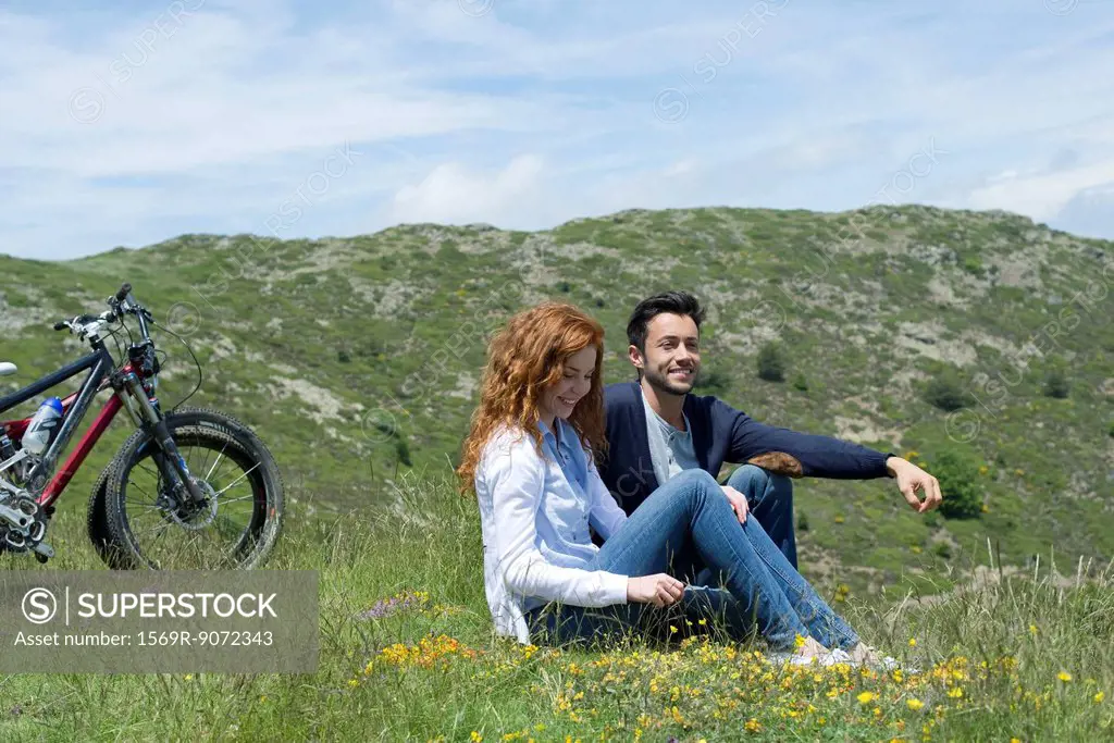 Couple sitting on meadow by mountain bikes