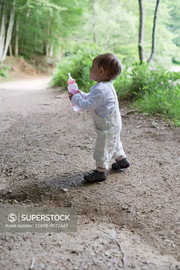 Baby girl holding baby bottle in woods