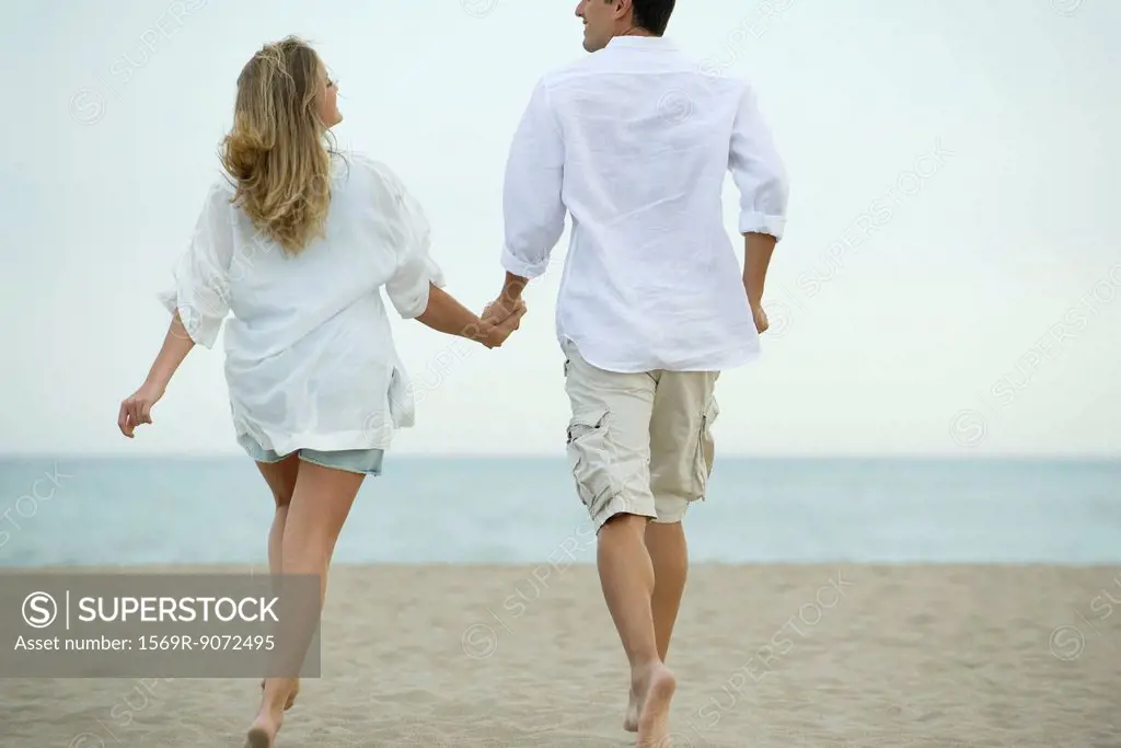Couple walking hand in hand on beach, rear view