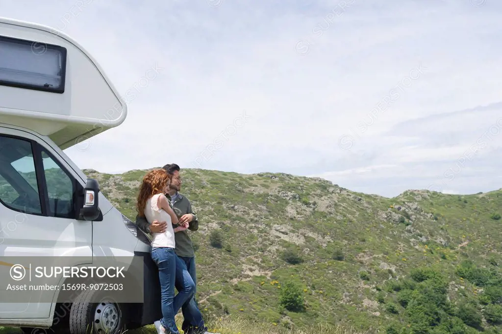 Couple embracing by motor home, enjoying scenic view