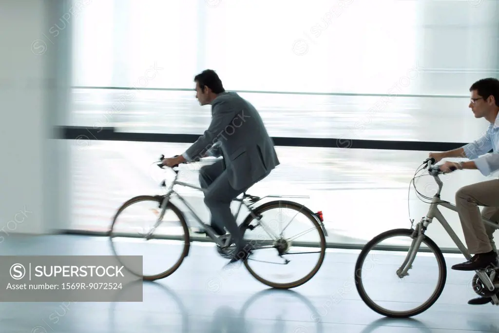 Businessmen riding bicycles indoors, silhouette, blurred motion