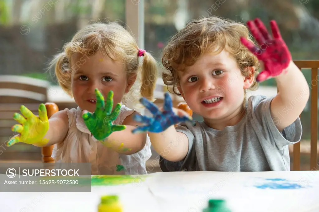 Little girl and boy showing hands covered in paint, portrait