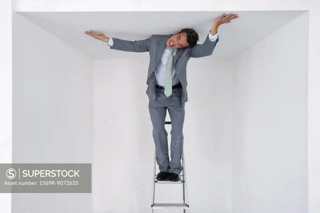 Executive standing on stepladder, pushing ceiling