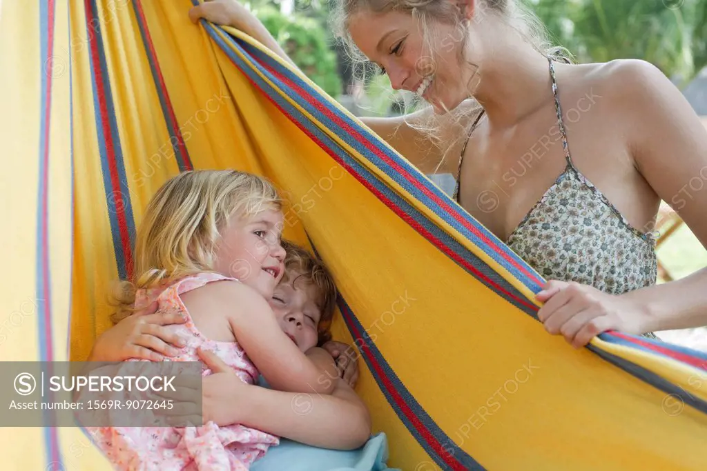 Mother watching as two young children embrace in hammock