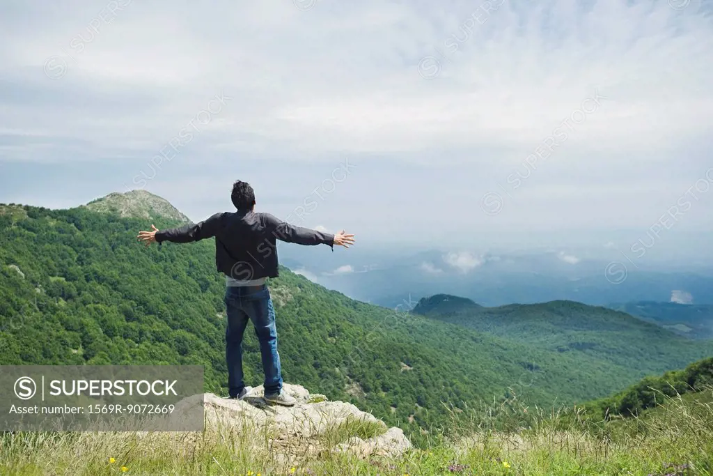 Man standing on top of rock with arms outstretched, rear view
