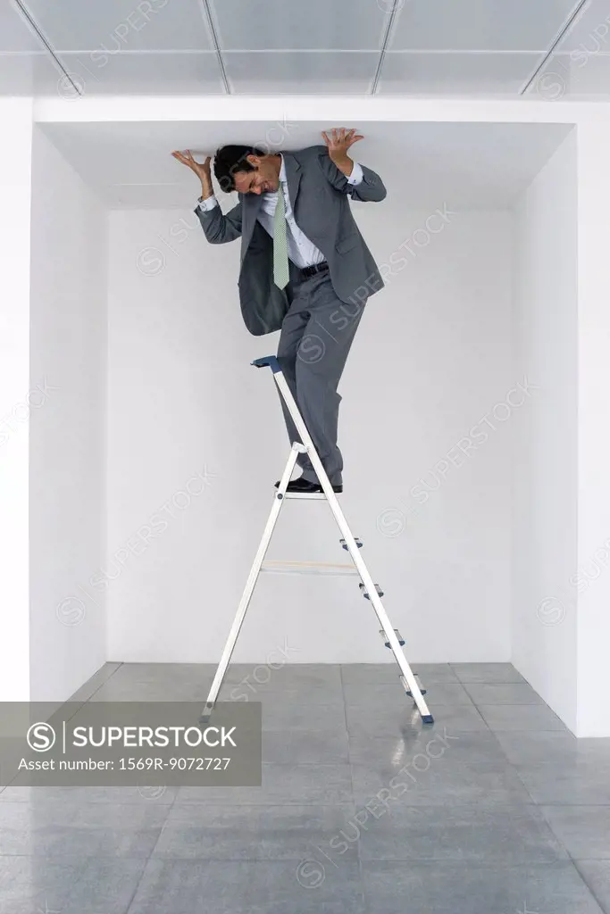 Executive standing on stepladder, pushing ceiling