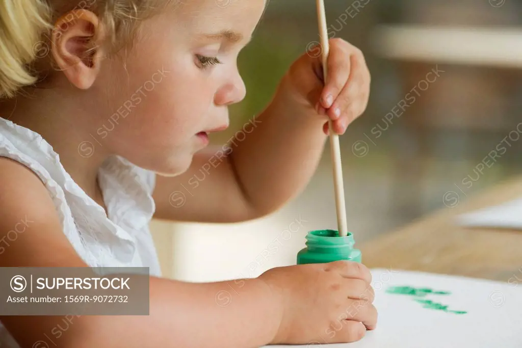 Little girl dipping paintbrush into paint