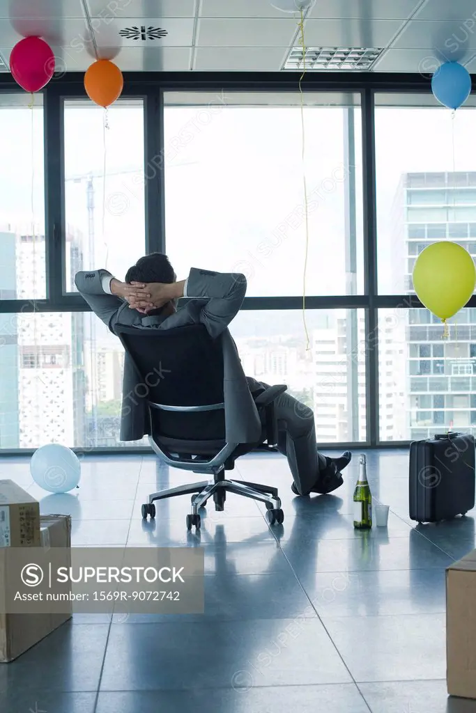 Businessman sitting in new office with balloons and boxes