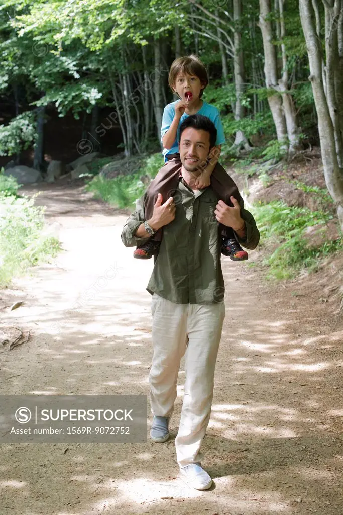 Father carrying son on shoulders, walking in woods